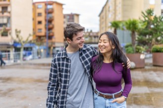 Multiethnic couple walks arm in arm, sharing a joyful moment in an urban setting. The scene