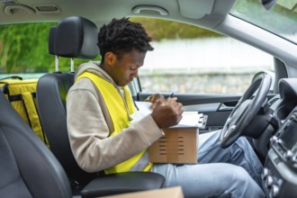 African delivery man checking packages for delivery sitting inside a car