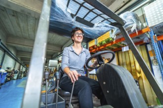 Happy female manual worker using forklift in a warehouse of a cnc metallurgic factory