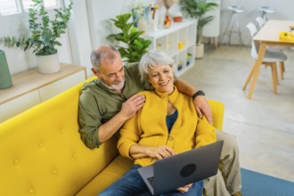 Elevated view photo of a casual senior couple lying on the sofa relaxed using laptop