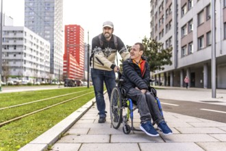 Caregiver pushing a smiling disabled man in a wheelchair along a bustling city sidewalk, enjoying a