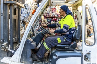 Side view full length photo of a latin man worker moving plastic bales driving forklift in a