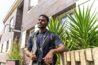 Portrait of a confident young african entrepreneur holding laptop waiting next to residential