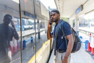 Casual african young businessman talking to the mobile while waiting for the train in the city