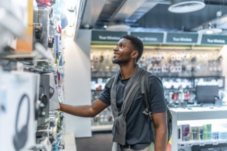 Side view photo with copy space of a young african man in a tech store looking at headphones