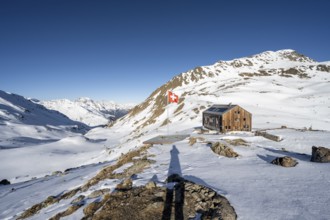 Swiss flag and mountain hut Keschhütte in front of mountain landscape in winter, behind summit of