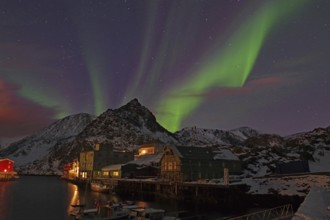 Night scene with northern lights in the sky, snow-covered mountains and houses by the water,