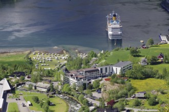 A large cruise ship is moored on a shore with many buildings and green meadows and trees, Geiranger