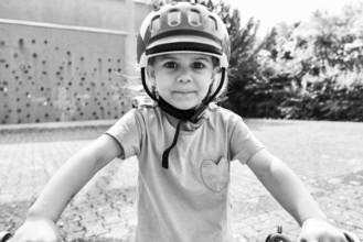 Child with helmet looking into the camera, a street in the background