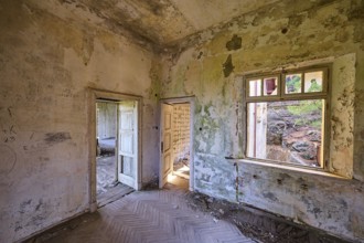 Dilapidated room with dirty walls, an open window and open door, showing green mould and