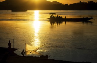 Fishermen fishing next to boats in the Brahmaputra river, during sunset in Guwahati, Assam, India