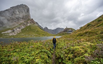 Mountaineer on hiking trail at Wolayersee, Alpine Club hut Wolayerseehütte, rocky cloudy mountains,