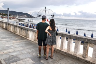 A couple with umbrella stands on the beach of Diana Marina, Italy, 18/08/2024, Diano Marina,
