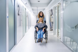 Nurse carrying a mature woman in wheelchair along the hospital corridor