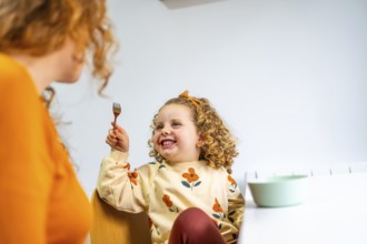 Playful girl eating and joking with her mother at home