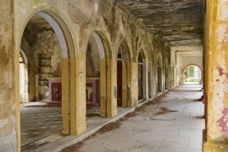 A dilapidated hall with arches and dirty walls, showing signs of neglect and wall decay, Italian