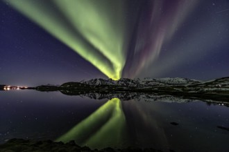 Yellow and green northern lights reflected in fjord, steep mountains, aurora borealis, winter,
