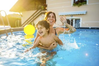 Happy mother and son are having fun, splashing and playing in a swimming pool during summer