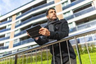Low angle view portrait of a casual adult caucasian businessman using digital tablet leaning on