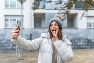 Caucasian young woman gesturing success while taking selfie in the city in winter