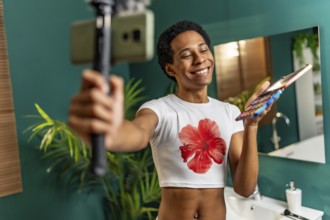 Happy latin gay man using mobile phone while recording makeup tutorial