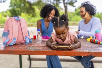 Little african girl using mobile phone in the park with her grandmother and mother talking on the