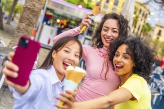 Three multi-ethnic female friends taking selfie while eating ice cream in the city