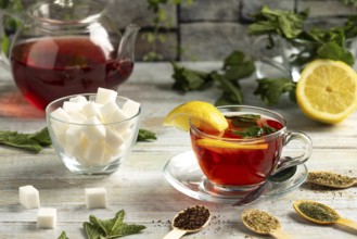Teapot and glass with tea, lemon and mint, next to sugar and teas on a table