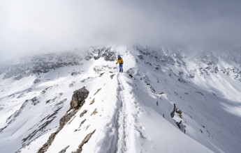 Mountaineer climbing up the narrow ridge of Piz Laviner, view of wintry mountain landscape, Grisons
