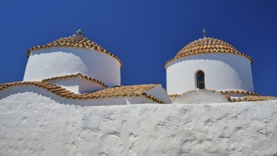 Two white painted church towers with red tiled roofs and small windows, bright blue sky, Chora, Old