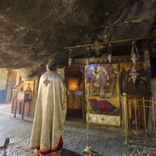 A clergyman stands in front of a scenic decorated room in a church during a service, rock grotto,