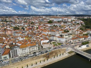 Wide angle shot of a city with tiled roofs and river, surrounded by hills and a sky with clouds,
