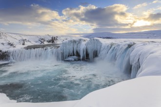 Icy waterfall and rapids in front of a mountain landscape, cloudy mood, snow, Godafoss, Isla