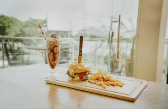 Close up of burger with fries and milkshake on wooden board with space for text. Delicious big