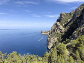Rugged cliffs overlooking the deep blue sea, crossed by a boat on the water, Cala d'en Sardina,