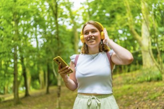 Young caucasian female tourist using phone and listening to music while hiking in the forest