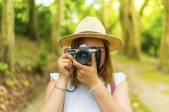 Frontal portrait of a caucacsian young woman traveler taking photos in the forest hiding with the