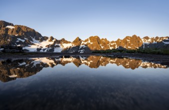 Rocky mountain peaks reflected in a small pond, mountain landscape with alpenglow at sunrise, at