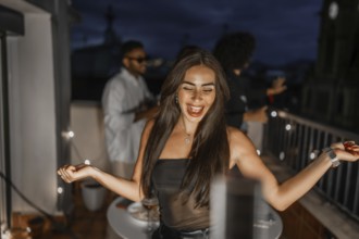 Happy woman dancing during night party on a city rooftop celebrating with multi-ethnic friends