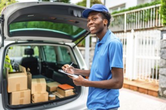 African delivery man in blue uniform verifying the packages on a van standing in the street