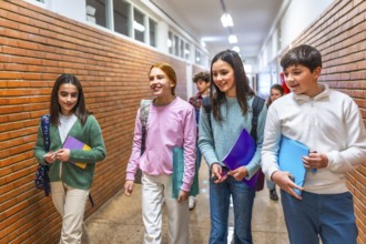 Cheerful students carrying books and folders are walking down school hallway between classes,