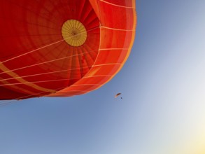 Hot air balloon ride, Paraglider with motor passes the hot air balloon. Background blue sky. Alice