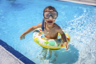 Happy playful caucasian boy with snorkel goggles and rubber ring on the swimming pool