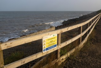 Environment Agency warning danger sign above rock armour, East Lane, Bawdsey, Suffolk, England, UK