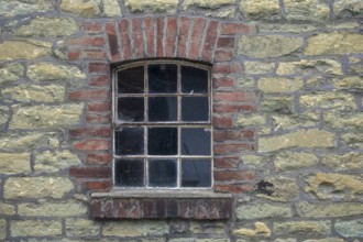 Single window embedded in a masonry stone wall with brick frame in an old farmhouse, North