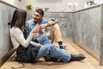 Two chefs are sitting on the floor of a modern kitchen, taking a break and chatting while enjoying
