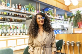 Beauty chic latin woman with curly hair and eyeglasses standing in a cafeteria smiling at camera