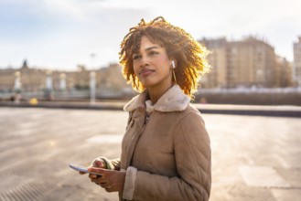 Latin beauty woman listening to music with earbuds and mobile phone outdoors in the city during