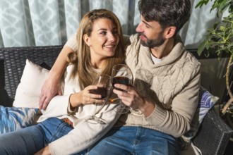 Romantic couple toasting with red wine, enjoying a cozy moment together on a comfortable sofa