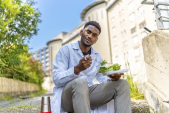 African young doctor sitting and eating healthy salad during a lunch break outside the hospital